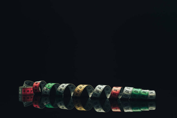 Measuring tape on a black glass table  beautiful dark  background  - unhealthy diet concept.