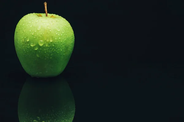 Green apple on a black glass table background.