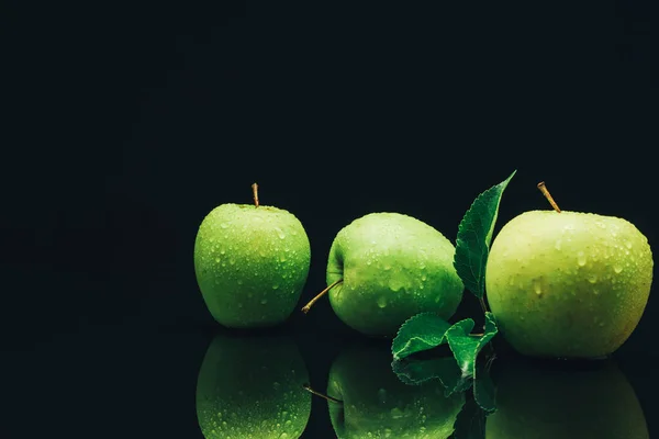 Three green apples on a black glass table background.