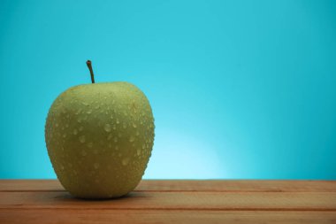 Kırmızı ahşap masada yeşil elma, mavi arka plan.