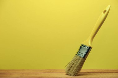 New paint brush on a Red Wooden Table. Beautiful yellow wall background behind. clipart