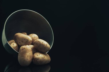 Siyah cam masa ve koyu arka plan üzerinde gümüş kase taze patates.