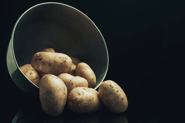 Fresh potato in silver bowl on a black glass table and dark background.