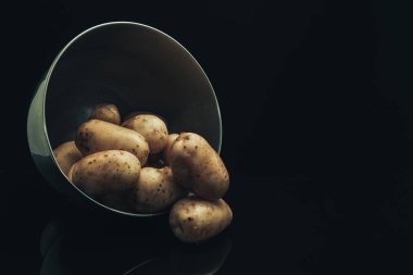 Siyah cam masa ve koyu arka plan üzerinde gümüş kase taze patates.