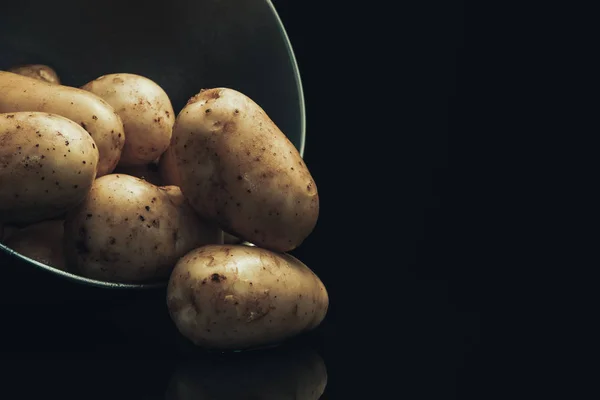 Close up fresh potato in silver bowl on a black glass table and dark background.