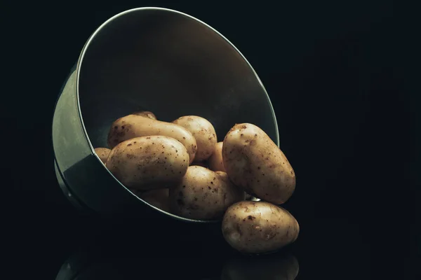 Fresh potato in silver bowl on a black glass table and dark background.
