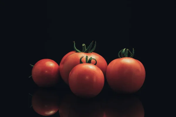 黒いガラスのテーブルと暗い背景に新鮮な4つのトマト — ストック写真