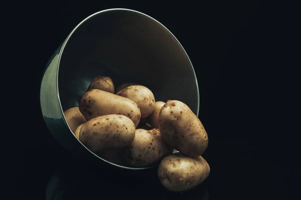 Close up fresh potato in silver bowl on a black glass table and dark background.