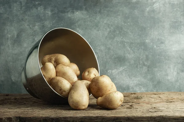 Fresh potato in silver bowl on a old oak wooden table and beautiful gray wall background.