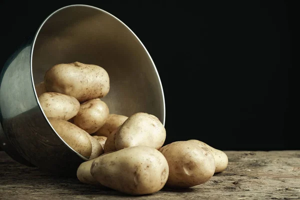 Fresh potato in silver bowl on a old oak wooden table and beautiful black background.