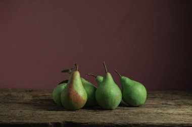 Eski bir meşe ahşap masa üzerinde taze yeşil armut, güzel kırmızı duvar arka plan.