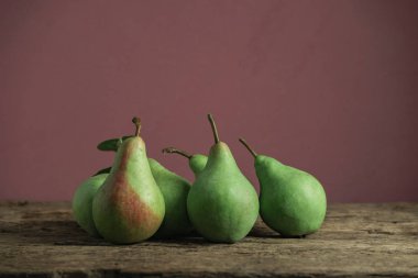 Eski bir meşe ahşap masa üzerinde taze yeşil armut, güzel kırmızı duvar arka plan.