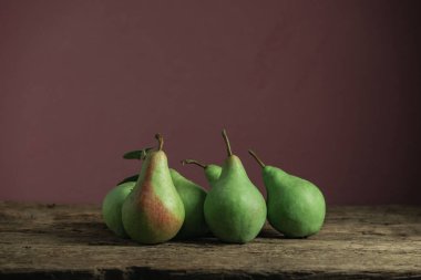 Eski bir meşe ahşap masa üzerinde taze yeşil armut, güzel kırmızı duvar arka plan.