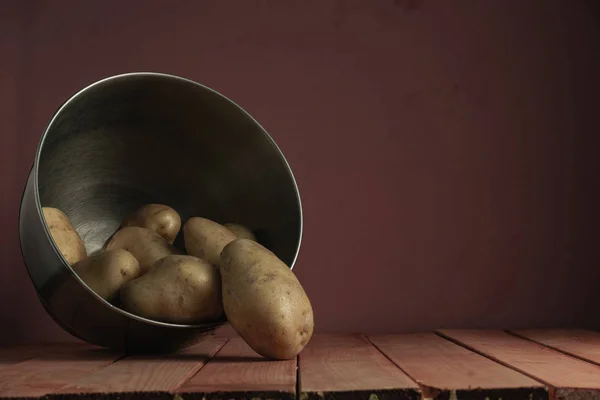 Fresh potatoes in silver bowl on a red wooden table and beautiful  dark-red wall background.
