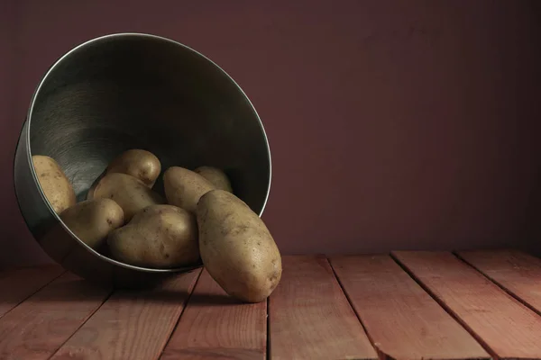 Fresh potatoes in silver bowl on a red wooden table and beautiful  dark-red wall background.