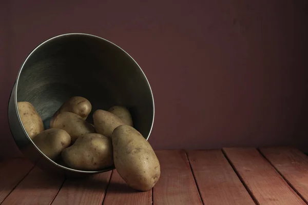Fresh potatoes in silver bowl on a red wooden table and beautiful  dark-red wall background.