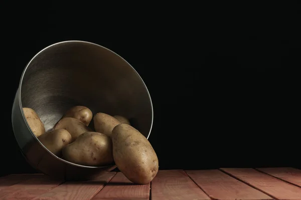 Fresh potato in silver bowl on a red wooden table and beautiful black background.