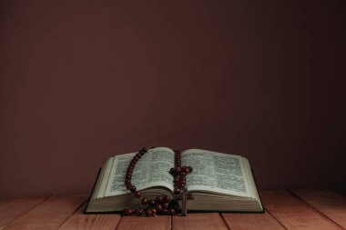 Kutsal Kitap'ı ve boncukları eski ahşap bir masanın üzerine açın. Güzel kırmızı duvar backgroround. Din kavramı.
