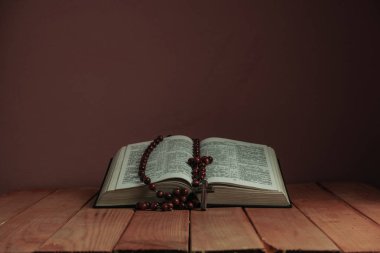 Kutsal Kitap'ı ve boncukları eski ahşap bir masanın üzerine açın. Güzel kırmızı duvar backgroround. Din kavramı.
