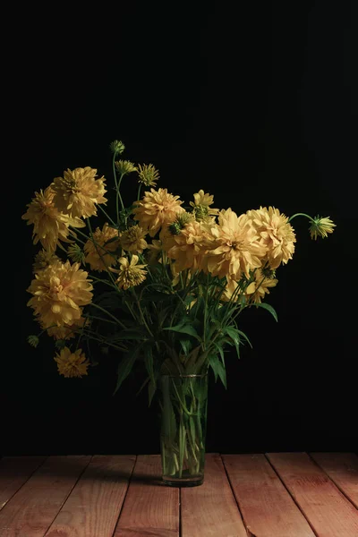 Yellow flowers in vase on a red wooden table and black background.
