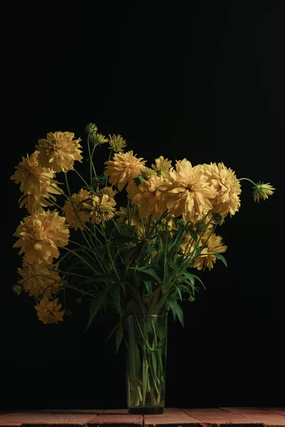 Yellow flowers in vase on a red wooden table and black background.