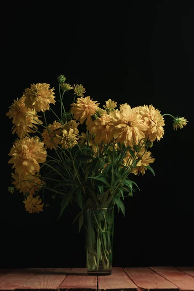 Yellow flowers in vase on a red wooden table and black background.