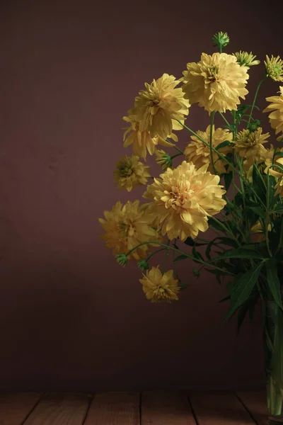 Yellow flowers in vase on a red wooden table, beautiful dark-red wall background.