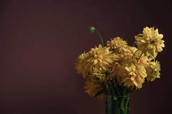 Yellow flowers in vase on a red wooden table, beautiful dark-red wall background.