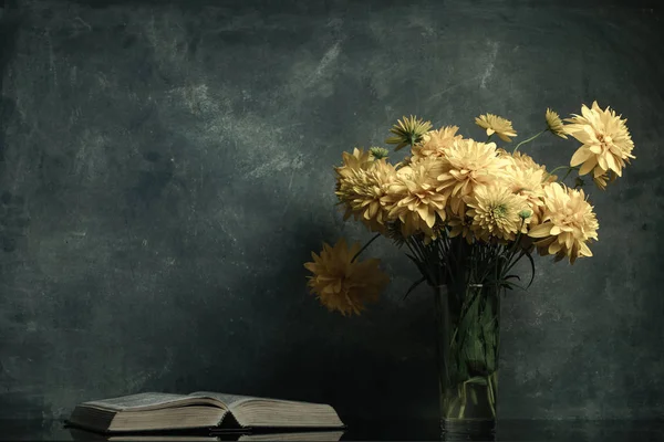Bible and yellow flowers in vase on a black glass table. Beautiful gray wall background