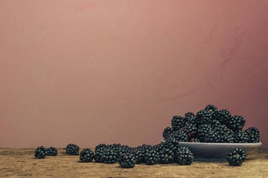 Eski bir meşe ahşap masa ve koyu kırmızı duvar arka plan üzerinde kase taze böğürtlen.