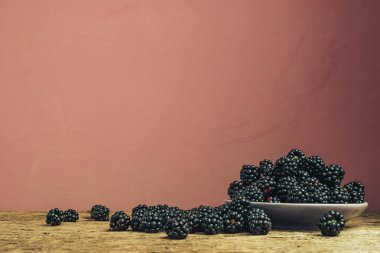 Eski bir meşe ahşap masa ve koyu kırmızı duvar arka plan üzerinde kase taze böğürtlen.