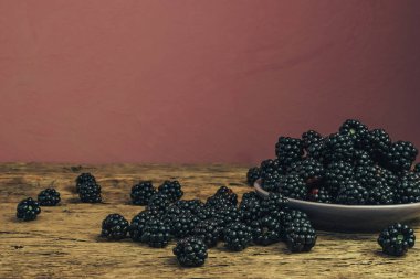 Eski bir meşe ahşap masa ve koyu kırmızı duvar arka plan üzerinde kase taze böğürtlen.