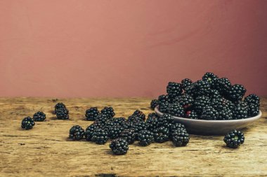 Eski bir meşe ahşap masa ve koyu kırmızı duvar arka plan üzerinde kase taze böğürtlen.