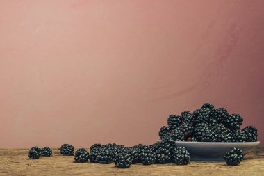 Eski bir meşe ahşap masa ve koyu kırmızı duvar arka plan üzerinde kase taze böğürtlen.