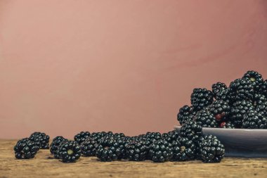 Eski bir meşe ahşap masa ve koyu kırmızı duvar arka plan üzerinde kase taze böğürtlen.