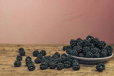 Eski bir meşe ahşap masa ve koyu kırmızı duvar arka plan üzerinde kase taze böğürtlen.