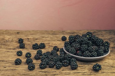 Eski bir meşe ahşap masa ve koyu kırmızı duvar arka plan üzerinde kase taze böğürtlen.