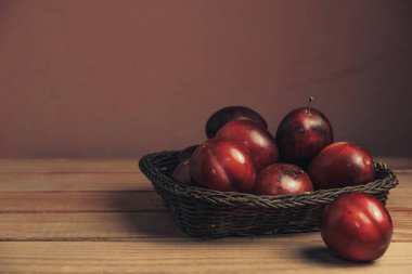 Kahverengi bir masada sepette taze kırmızı erik. Güzel koyu kırmızı duvar arka plan.