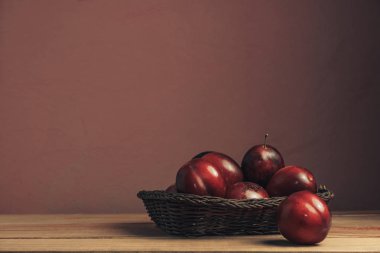 Kahverengi bir masada sepette taze kırmızı erik. Güzel koyu kırmızı duvar arka plan.