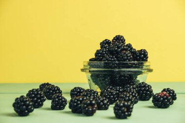 Yeşil ahşap masa ve sarı duvar arka plan üzerinde cam kase taze böğürtlen.