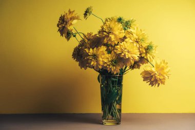 Bir masa ve sarı duvar arka plan üzerinde vazo sarı çiçekler.