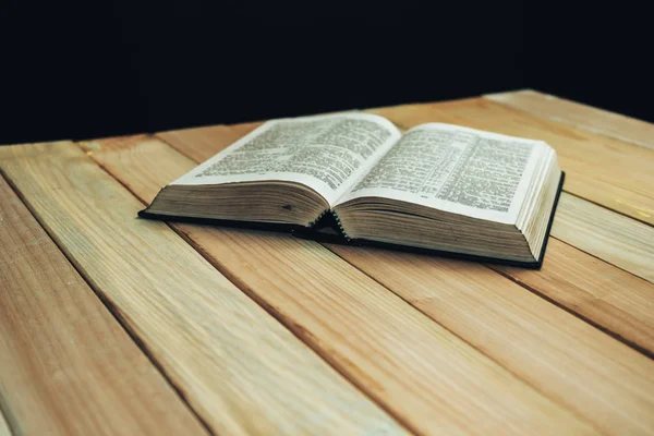 Open Bible book on a wooden table and black background.