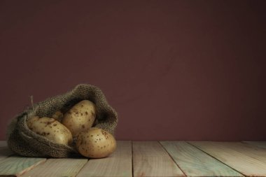 Ahşap masada ve güzel koyu kırmızı duvar arka planda torbada taze patates.