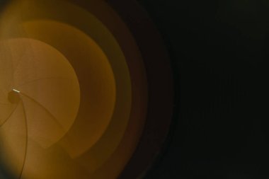 Siyah zemin üzerinde sarı ışık yansıması olan güzel bir kamera lensi.