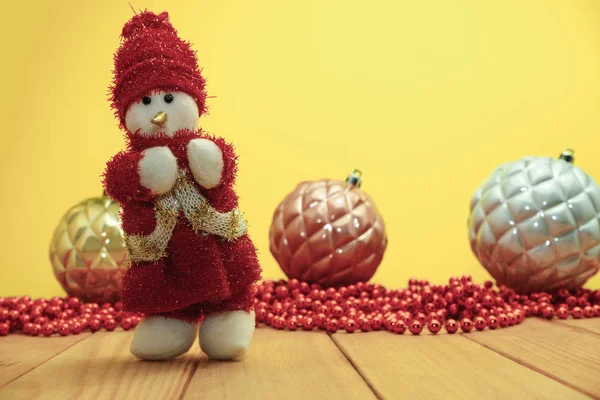 Güzel Noel baubles kardan adam kırmızı ahşap masa ve sarı arka plan üzerinde Noel Baba giyinmiş.