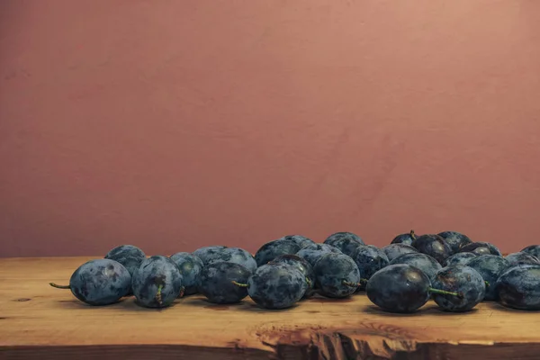 Beautiful fresh blue plums on brown wooden table and red wall background.