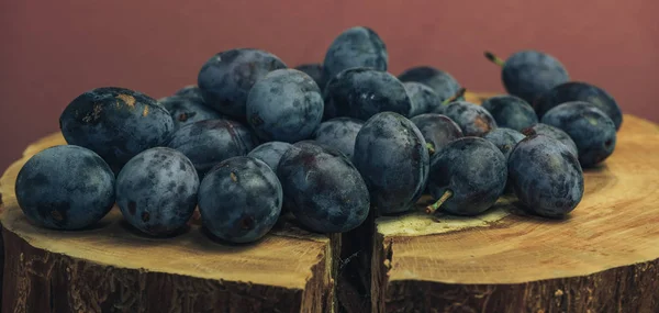 Beautiful fresh blue plums on a tree stump and red wall background.