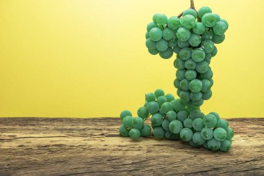 Eski bir meşe ahşap masa ve sarı duvar arka plan üzerinde güzel taze beyaz asma üzüm.