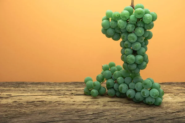 Eski bir meşe ahşap masa ve turuncu duvar arka plan üzerinde güzel taze beyaz asma üzüm.