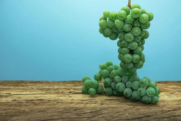 Eski bir meşe ahşap masa ve mavi duvar arka plan üzerinde güzel taze beyaz asma üzüm.